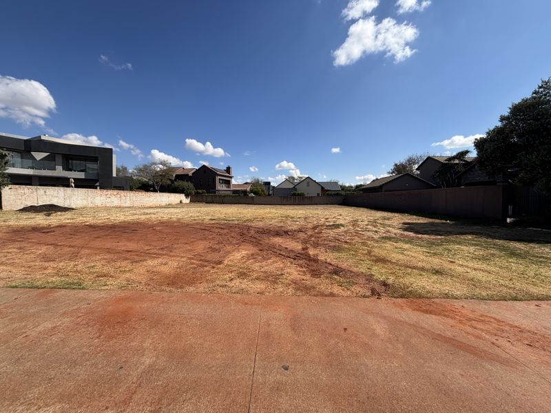 A vacant residential plot featuring a concrete driveway and perimeter walling, situated in a developed neighborhood.