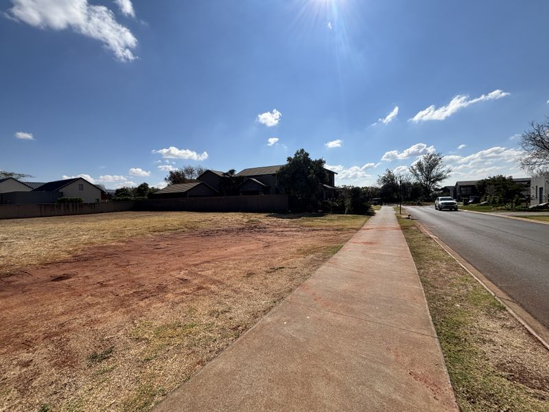 A vacant residential plot featuring a paved sidewalk and boundary wall, situated in a developed neighborhood.