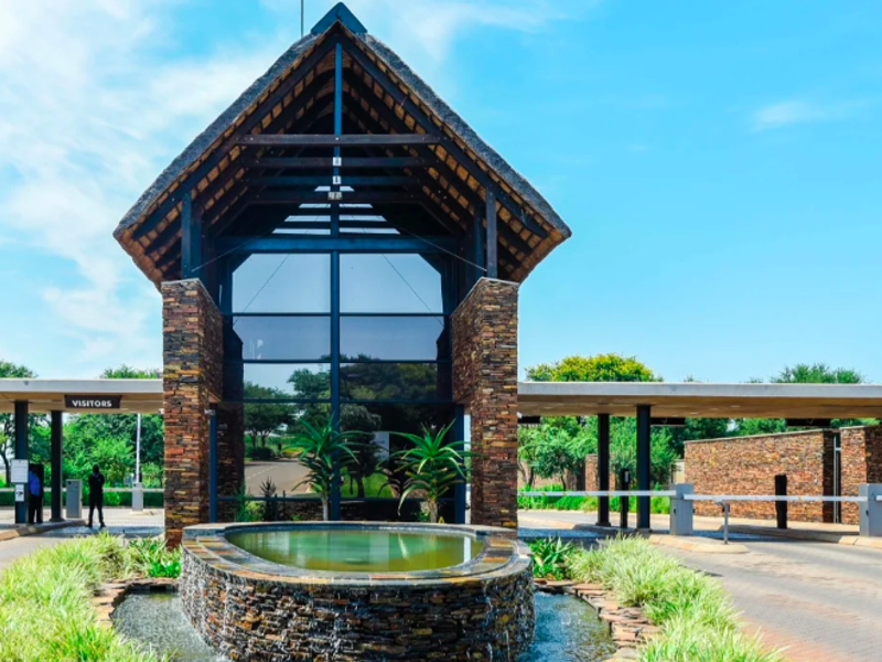 Main entrance gatehouse of the residential estate featuring stone cladding, a thatched roof, a central water feature, and secure visitor access control points.