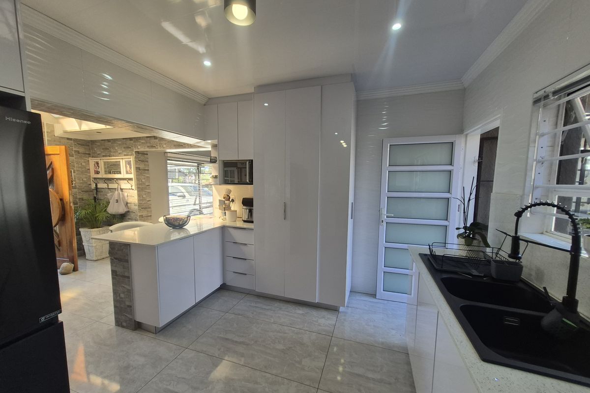 Modern kitchen featuring high-gloss white cabinetry, stone countertops, a double basin sink with a gooseneck tap, and integrated microwave, finished with tiled flooring.