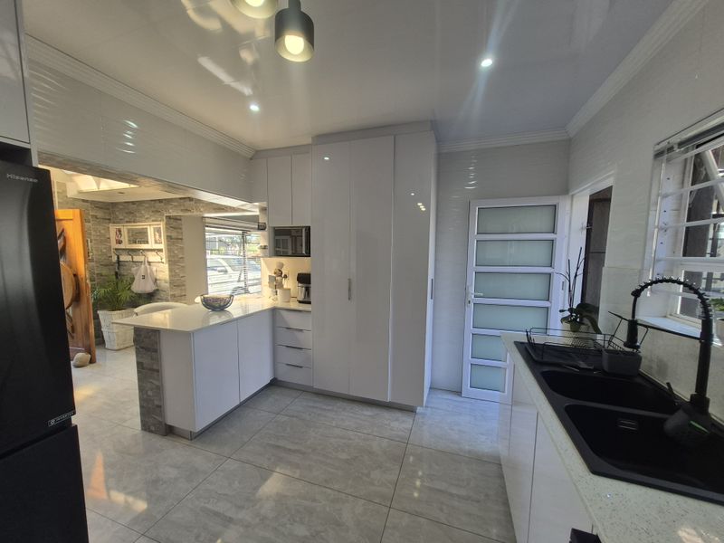 Modern kitchen featuring high-gloss white cabinetry, stone countertops, a double basin sink with a gooseneck tap, and integrated microwave, finished with tiled flooring.