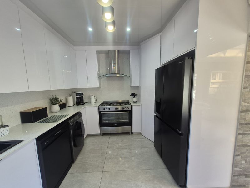 Modern kitchen featuring high-gloss white cabinetry, stone countertops, stainless steel appliances, and sleek porcelain floor tiles with recessed lighting.