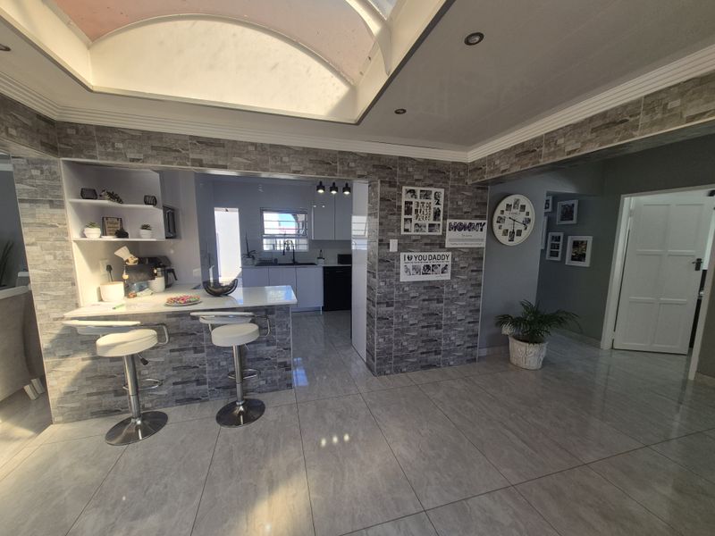 Modern open-plan living area featuring stone veneer wall accents, a large skylight, and polished porcelain floor tiles, seamlessly connecting to the kitchen space.