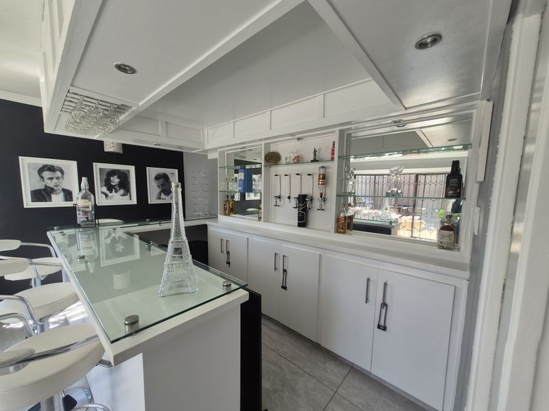 A well-appointed built-in home bar featuring a glass-topped counter, custom white cabinetry, mirrored shelving, and recessed ceiling lighting.
