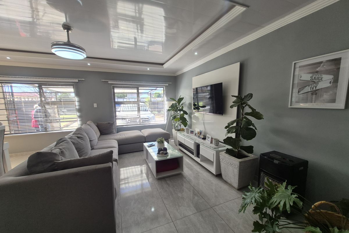 A well-maintained living room featuring glossy tiled floors, a modern recessed ceiling with crown molding, and a built-in media wall panel.