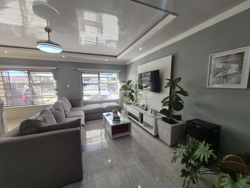 A well-maintained living room featuring glossy tiled floors, a modern recessed ceiling with crown molding, and a built-in media wall panel.