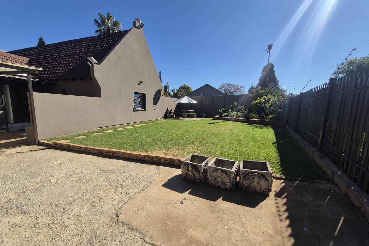 A spacious rear garden featuring a well-maintained lawn, brick-edged borders, and a concrete driveway area, enclosed by perimeter fencing.