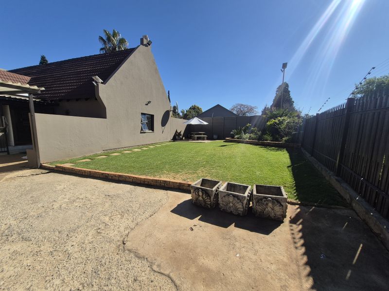 A spacious rear garden featuring a well-maintained lawn, brick-edged borders, and a concrete driveway area, enclosed by perimeter fencing.