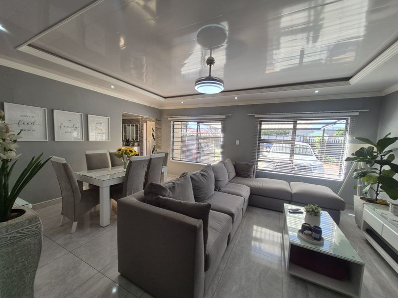 Spacious open-plan living and dining area featuring glossy ceilings, recessed lighting, tiled floors, and large windows with venetian blinds.