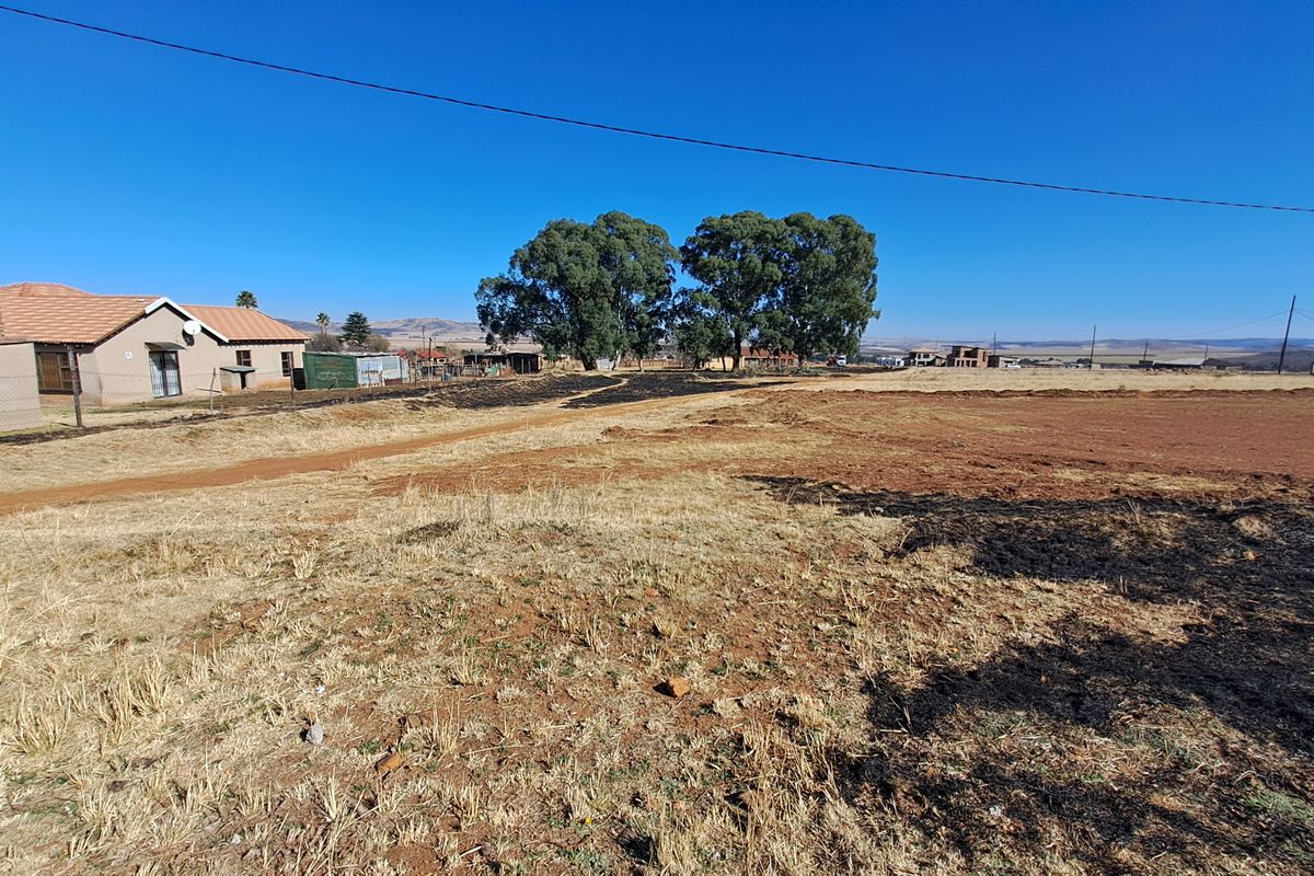 A wide-angle view of a vacant residential plot featuring dry, unmaintained land with a dirt access path and surrounding rural landscape.