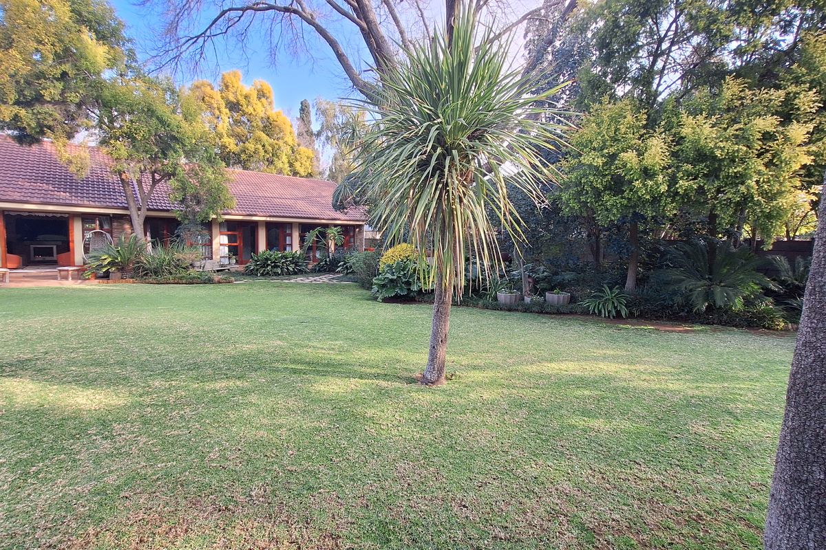 A spacious, well-maintained rear garden featuring a lush lawn, mature trees, and a covered patio area attached to the main residence.