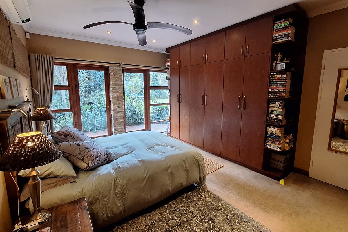 A well-maintained bedroom featuring extensive built-in wooden cabinetry, a ceiling fan, air conditioning, and large sliding glass doors providing garden views.