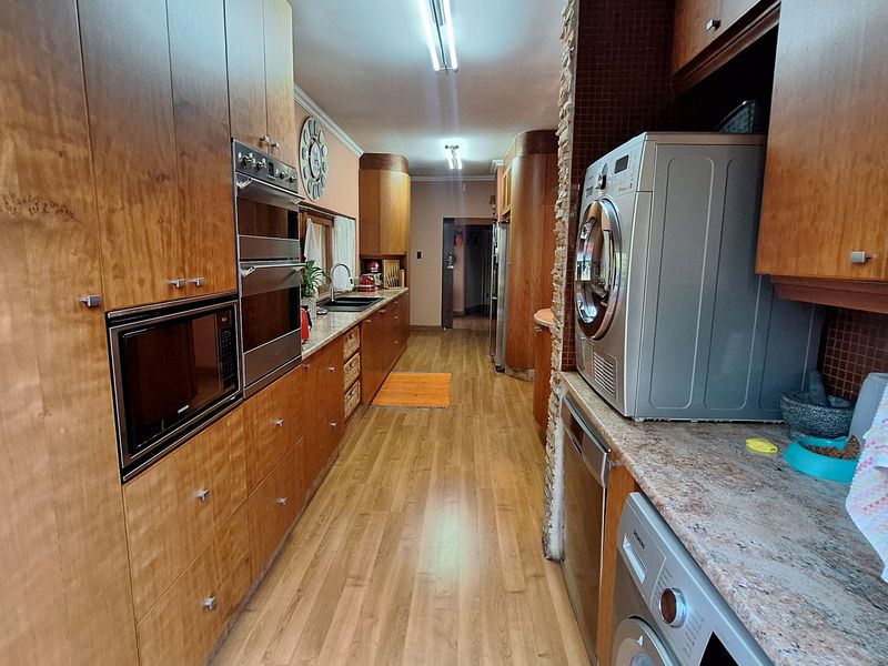 A galley-style kitchen featuring extensive wooden cabinetry, built-in double ovens, a microwave, and laminate countertops with integrated sink and laundry appliance space.