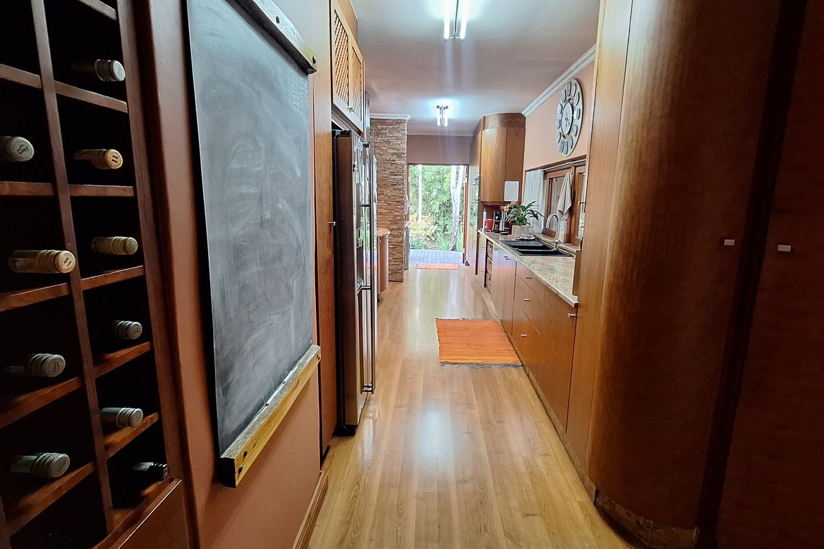 A galley-style kitchen featuring extensive wooden cabinetry, stone countertops, a double sink, and a built-in wine rack, leading to an outdoor area.