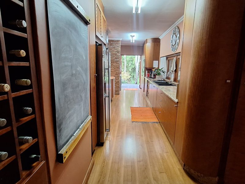 A galley-style kitchen featuring extensive wooden cabinetry, stone countertops, a double sink, and a built-in wine rack, leading to an outdoor area.