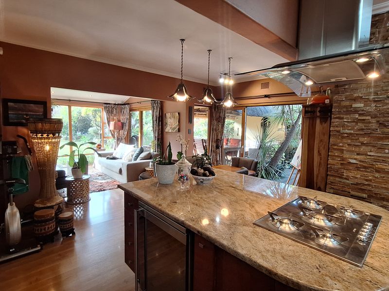 Spacious open-plan kitchen and living area featuring a granite island with gas cooktop, stacked stone accents, and seamless flow to the outdoor patio.