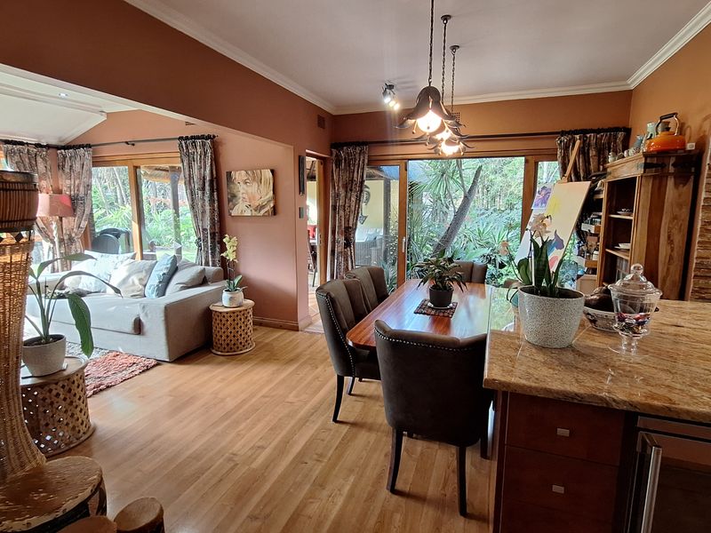 Spacious open-plan living and dining area featuring hardwood floors, granite kitchen countertops, a stone feature wall, and large sliding doors opening to the garden.