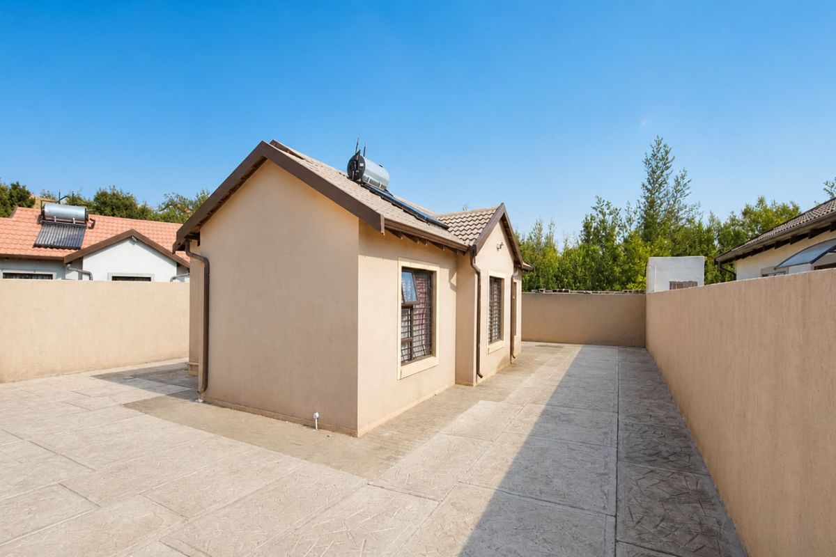 A rear view of the property featuring a paved courtyard, perimeter boundary walls, and a solar water heating system installed on the tiled roof.