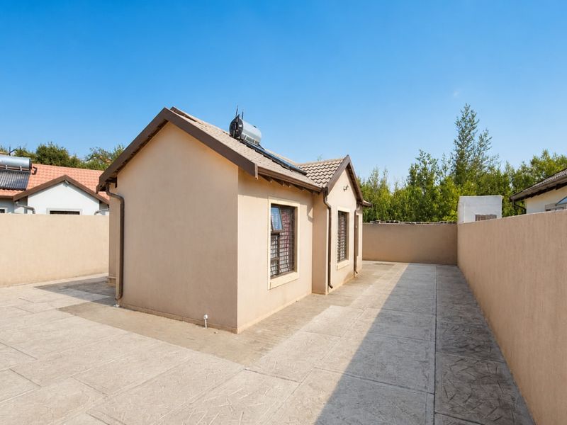 A rear view of the property featuring a paved courtyard, perimeter boundary walls, and a solar water heating system installed on the tiled roof.