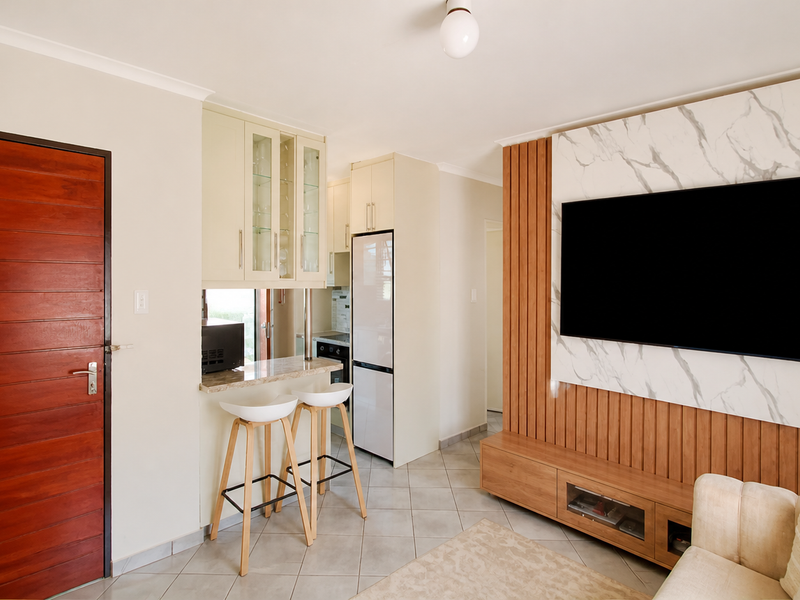Modern open-plan living area featuring a sleek kitchen nook with stone countertops and a stylish marble and timber slat media wall.