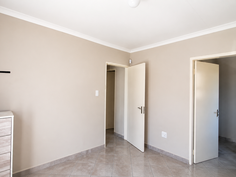 A clean, neutral-toned bedroom featuring tiled flooring, coved ceilings, and direct access to adjacent rooms.