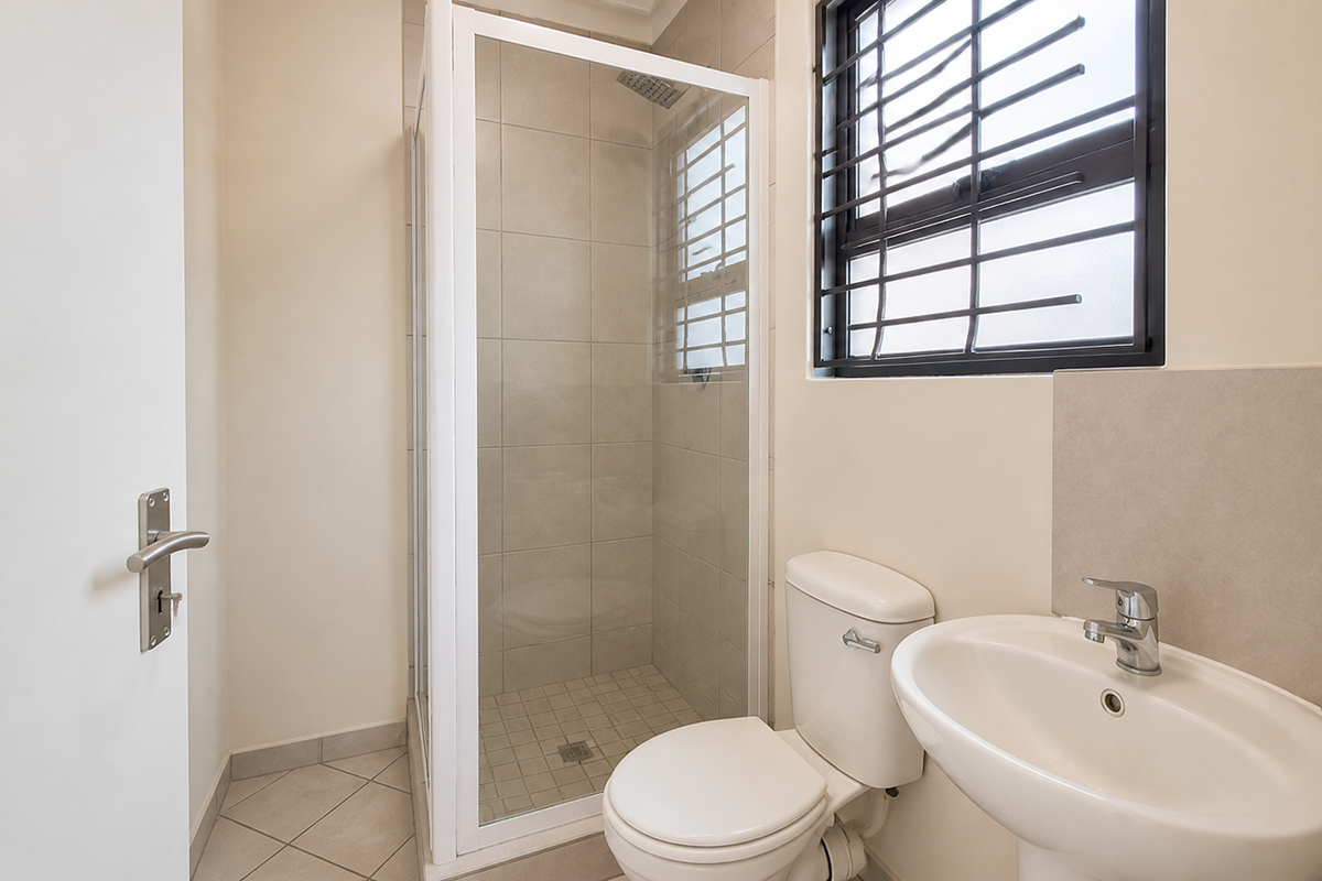 A clean and functional bathroom featuring a glass shower enclosure, pedestal basin, and toilet with neutral wall and floor tiling.