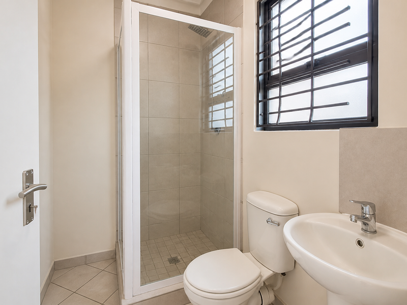 A clean and functional bathroom featuring a glass shower enclosure, pedestal basin, and toilet with neutral wall and floor tiling.
