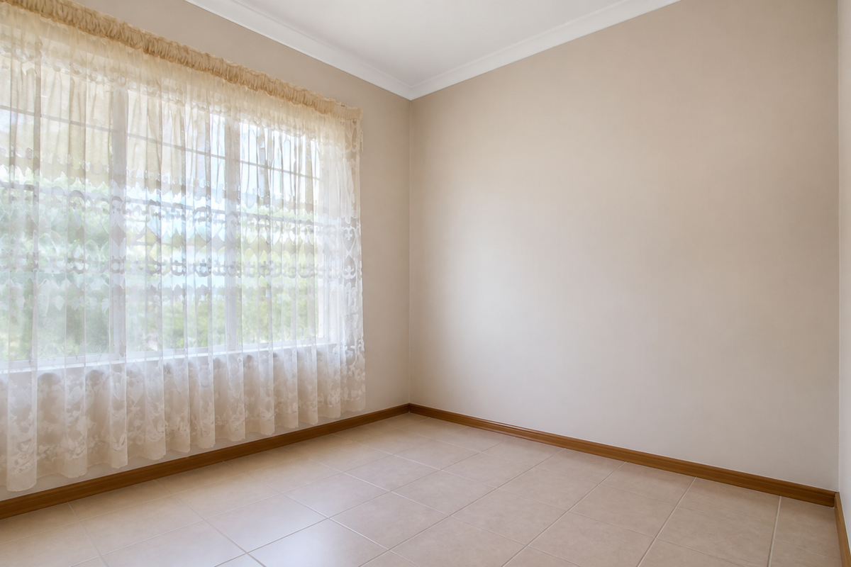 A bright, empty bedroom featuring neutral tiled flooring, clean walls, and a large window with natural light.