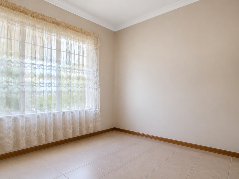 A bright, empty bedroom featuring neutral tiled flooring, clean walls, and a large window with natural light.