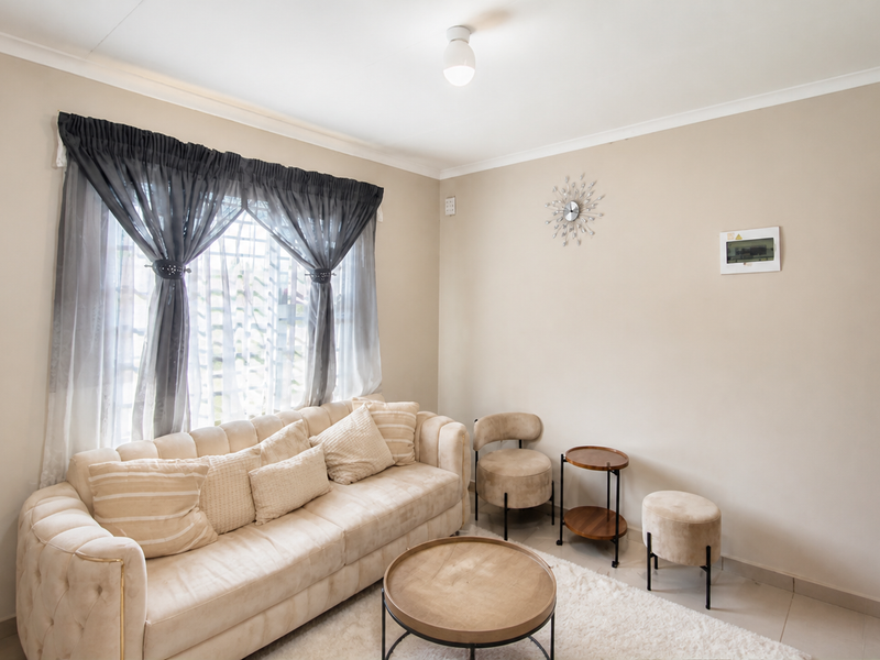 A well-maintained living room featuring neutral wall tones, tiled flooring, and decorative cove cornicing, providing a bright and comfortable living space.