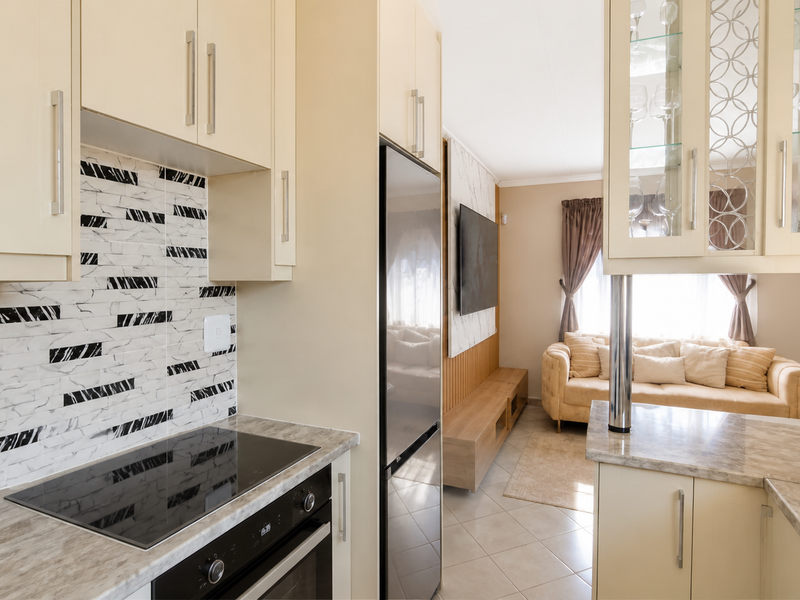 Open-plan kitchen and living area featuring modern cabinetry, stone countertops, integrated appliances, and a decorative backsplash, flowing into a comfortable lounge space.