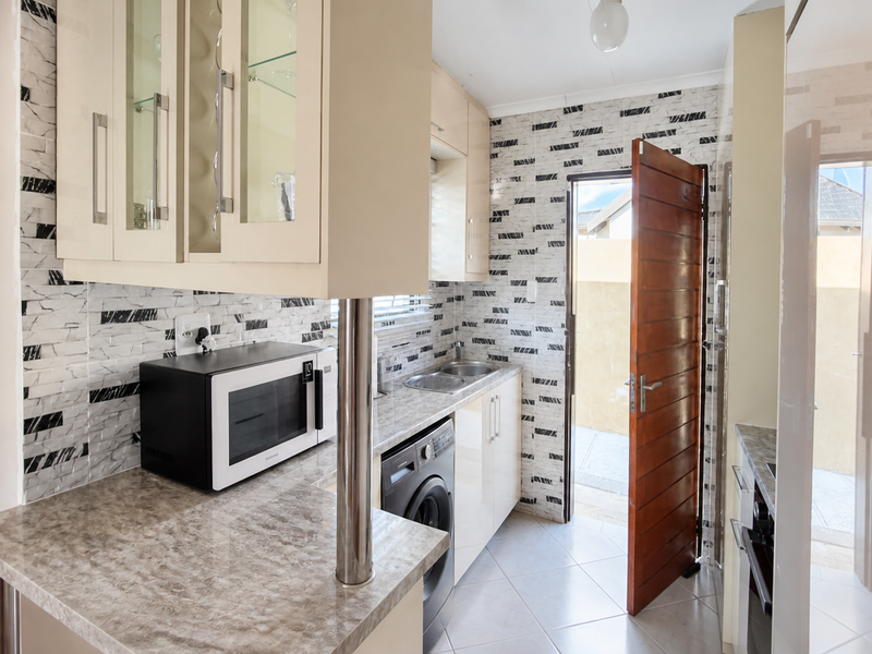 A functional scullery featuring built-in cabinetry, laminate countertops, a stainless steel sink, and tiled finishes, with direct access to the exterior.