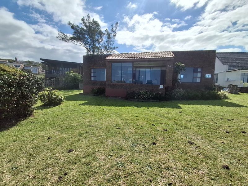 Rear view of a face brick house featuring a tiled roof, large windows, and a spacious surrounding lawn area.