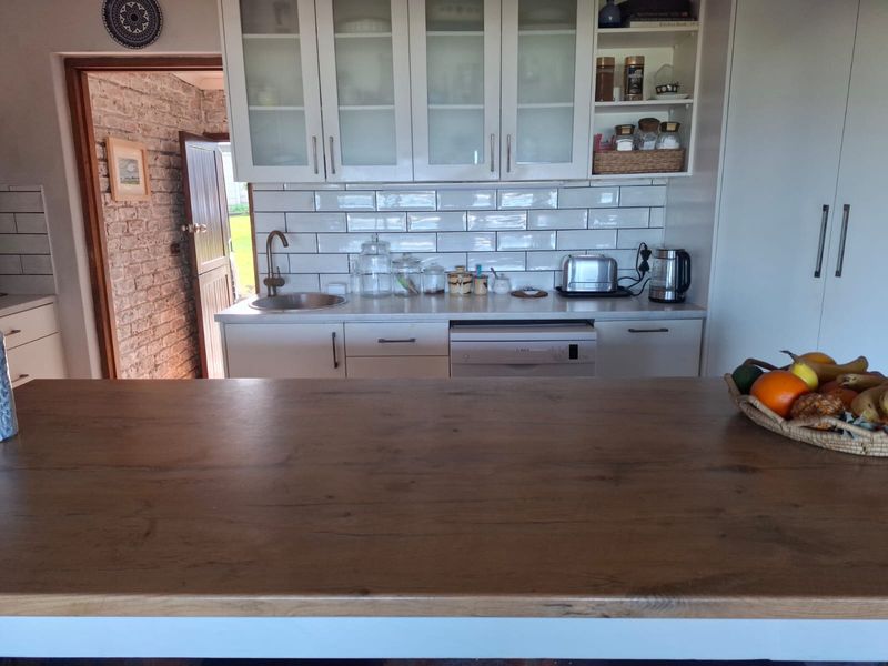 A well-maintained kitchen featuring white cabinetry, a subway tile backsplash, wooden countertops, and an integrated dishwasher, with an adjacent brick-walled entryway.