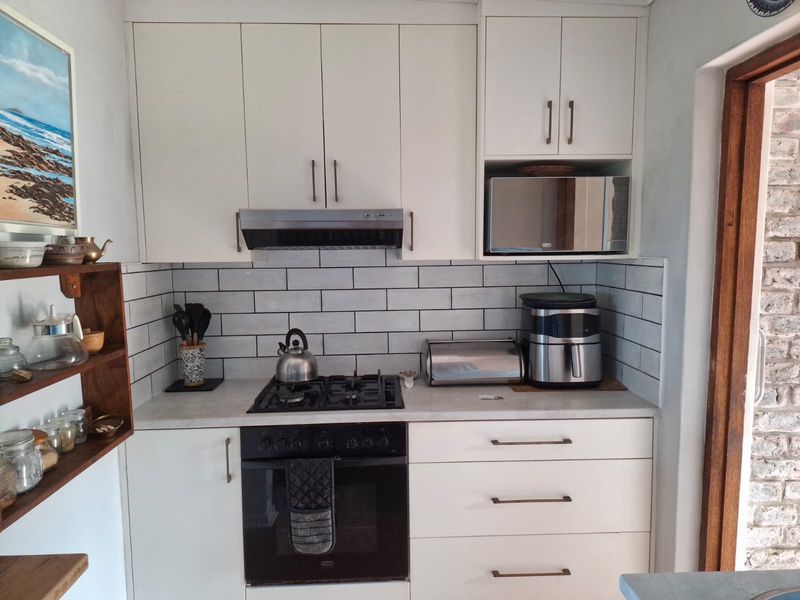 A well-maintained kitchen featuring white cabinetry, a subway tile backsplash, and integrated appliances including a gas hob, oven, and microwave.
