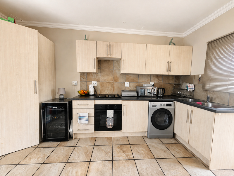 Functional kitchen featuring light wood cabinetry, stone-look tile backsplash, ceramic flooring, and integrated appliances including an oven, hob, and washing machine.