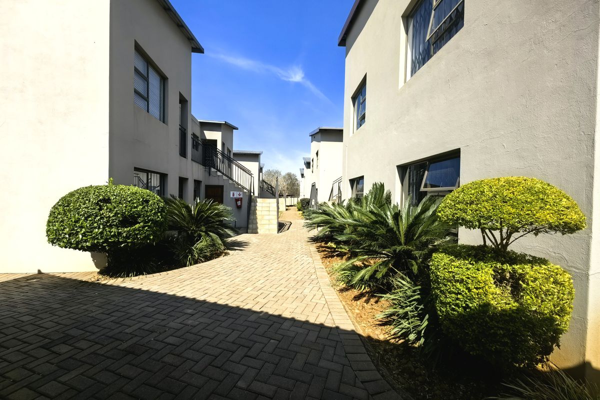 A well-maintained paved walkway between apartment blocks featuring landscaped shrubs and external building access points.