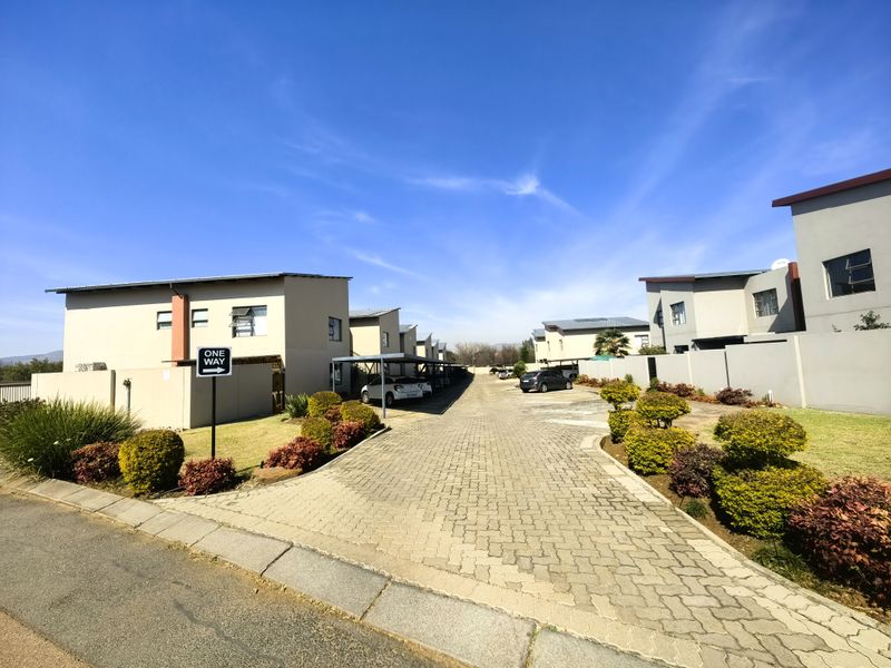 View of the apartment complex driveway featuring paved access, covered parking bays, and well-maintained boundary walls with landscaped garden beds.