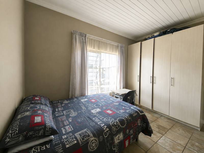 A functional bedroom featuring built-in cupboards, tiled flooring, and a timber ceiling, providing a practical living space with natural light.