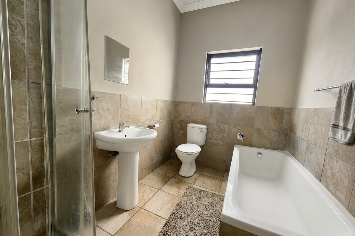 A functional bathroom featuring a pedestal basin, toilet, bathtub, and a separate glass-enclosed shower with neutral tiled finishes throughout.