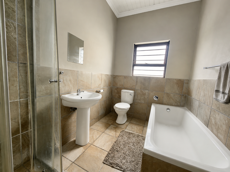 A functional bathroom featuring a pedestal basin, toilet, bathtub, and a separate glass-enclosed shower with neutral tiled finishes throughout.