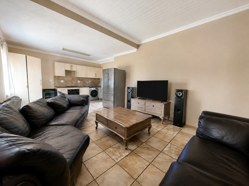 Open-plan living area featuring tiled flooring, a functional kitchen with built-in cabinetry, and a classic tongue and groove ceiling finish.
