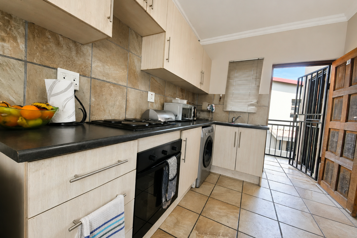 Functional kitchen featuring light wood-finish cabinetry, dark countertops, tiled backsplash, and direct access to an outdoor balcony area.