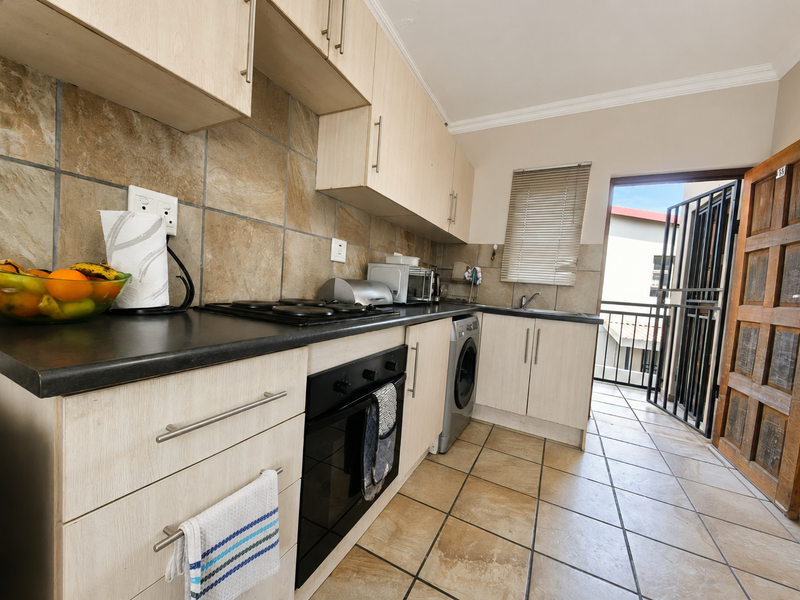 Functional kitchen featuring light wood-finish cabinetry, dark countertops, tiled backsplash, and direct access to an outdoor balcony area.