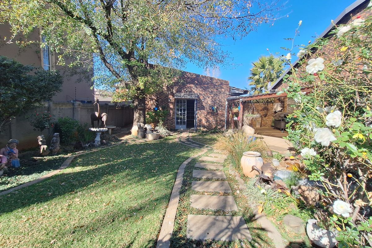 A rear garden area featuring a paved walkway, established lawn, and a covered patio space adjacent to the main building structure.