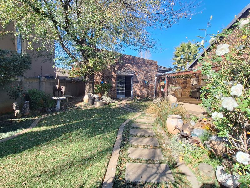 A rear garden area featuring a paved walkway, established lawn, and a covered patio space adjacent to the main building structure.