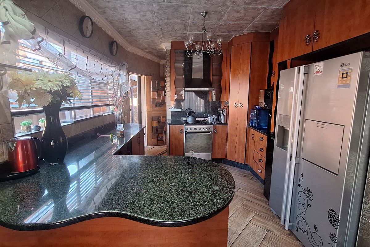 A functional kitchen featuring granite countertops, wooden cabinetry, a stainless steel extractor fan, and tiled flooring with a distinct textured ceiling finish.