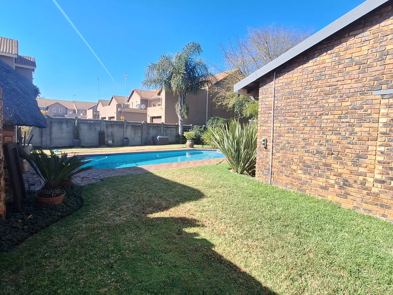 A private backyard featuring a swimming pool, paved surround, and established garden area enclosed by brick boundary walls.