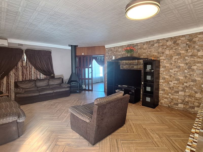 Spacious living room featuring herringbone tile flooring, a stone veneer feature wall, and a freestanding fireplace, offering a comfortable and functional living space.
