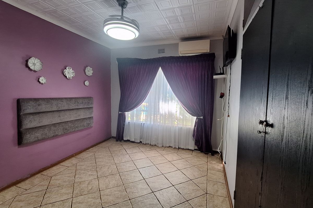 A spacious bedroom featuring tiled flooring, a built-in cupboard, a ceiling fan, and a wall-mounted air conditioning unit.